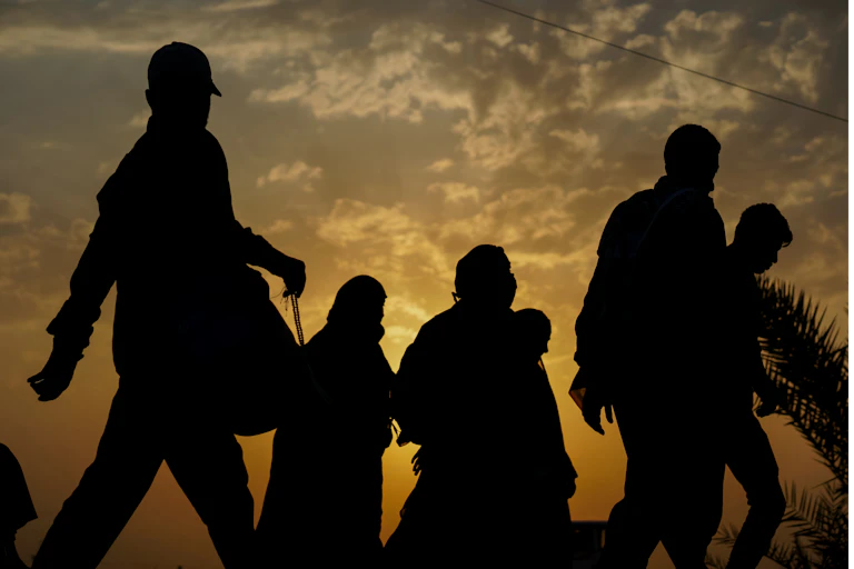 Silhouetted against a fading sunset, a group of immigrants walk with their belongings.