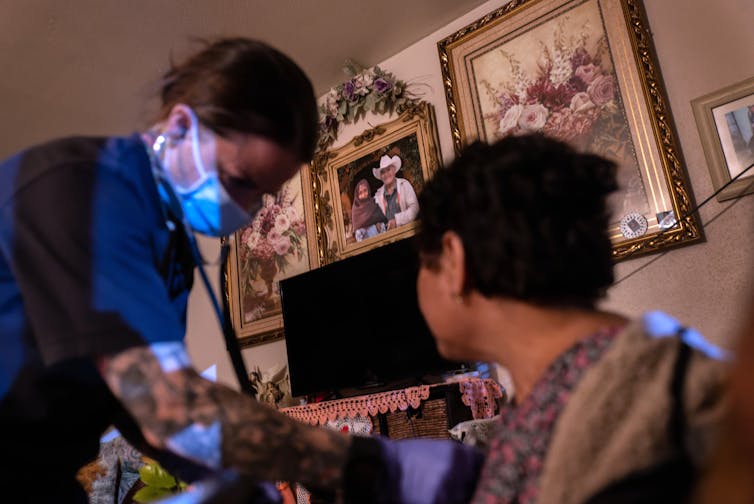 A medic, dressed in blue garb and wearing a mask, takes a patient's blood pressure.