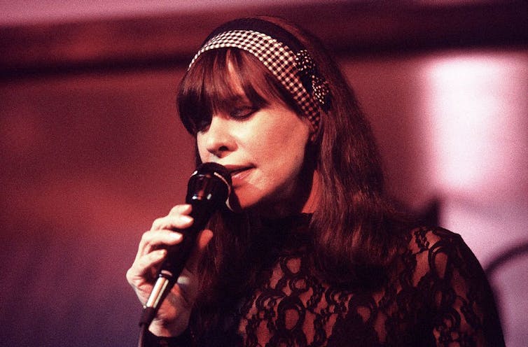 Woman bathed in magenta light closes her eyes while singing.