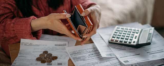 Woman holding empty purse open, surrounded by paperwork, a pile of coins, calculator.
