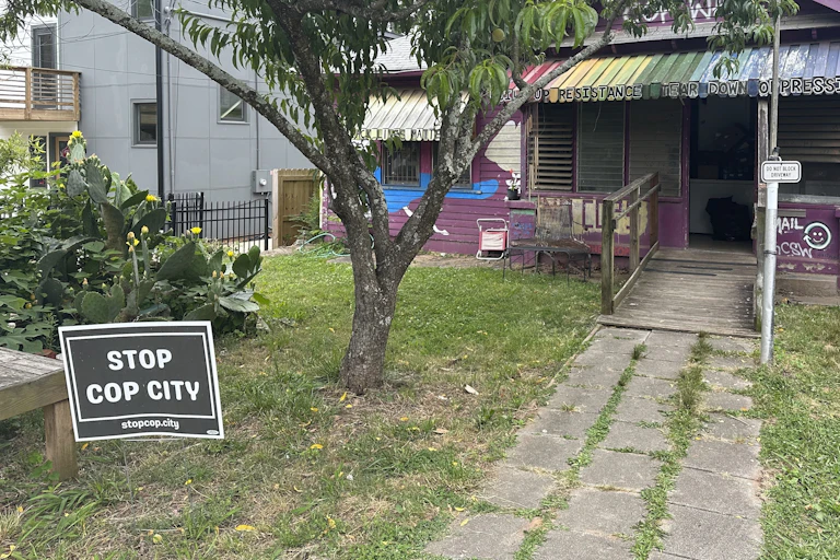 Small, modest house with a rainbow-painted awning and a 'Stop Cop City' sign in the yard.