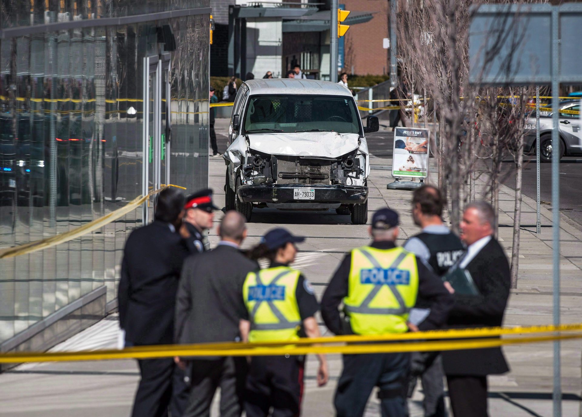 Police stand in front of a damaged van on a city sidewalk.
