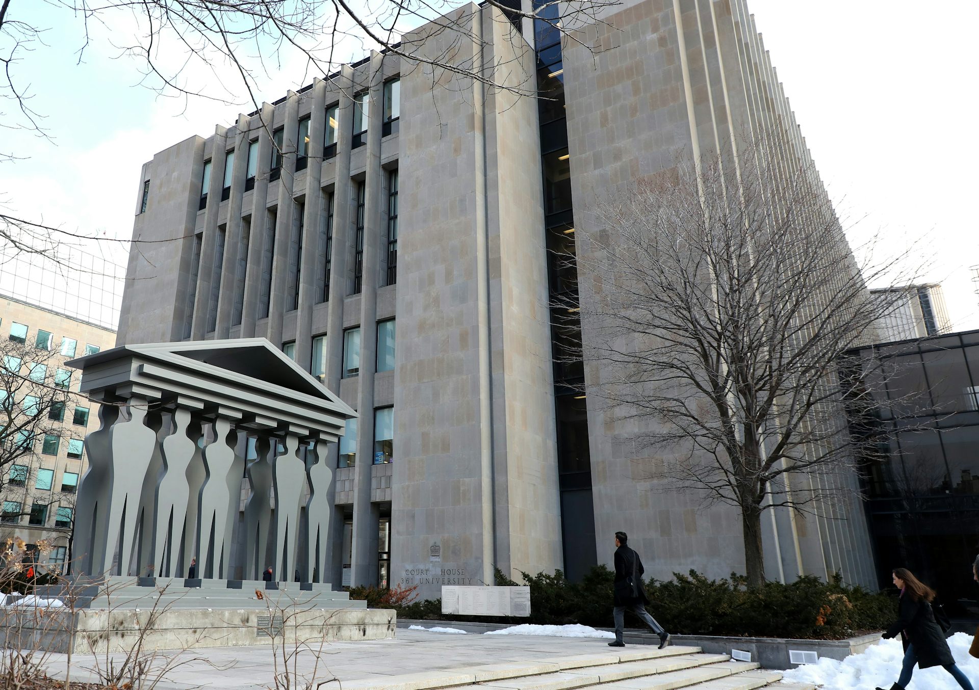 A grey government building next to a monument made of grey human figures.