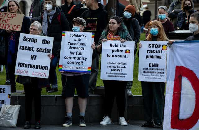 People at a rally stand together holding signs protesting racial inequities in Australia. 