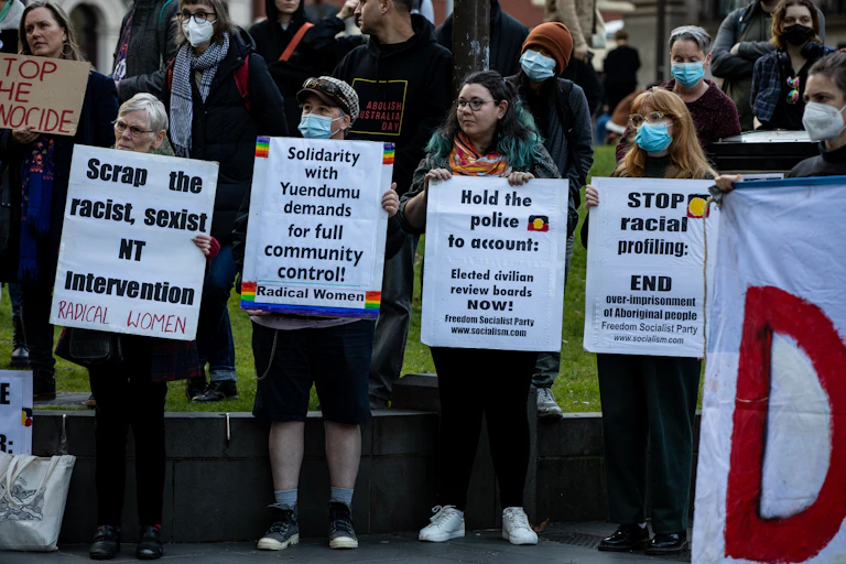 People at a rally stand together holding signs protesting racial inequities in Australia.