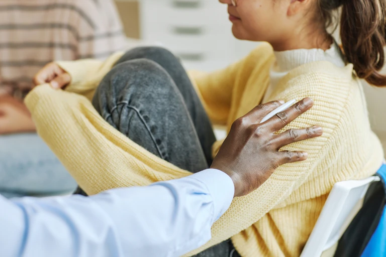 Hand on shoulder of teenager, sitting with knees up and arms around knees