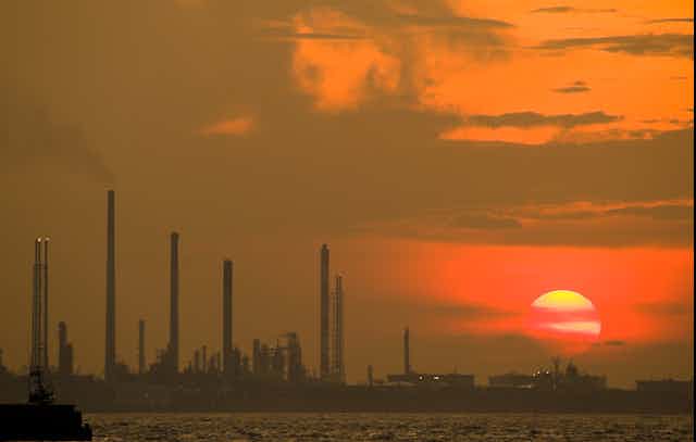 Sun setting in orange haze above industrial scene.
