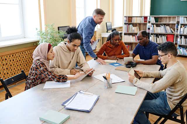 Un grupo de personas de diferentes etnias estudia y charla alrededor de una mesa.