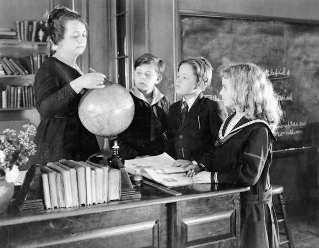 Una maestra enseña geografía con una bola del mundo ante tres alumnos de uniforme.