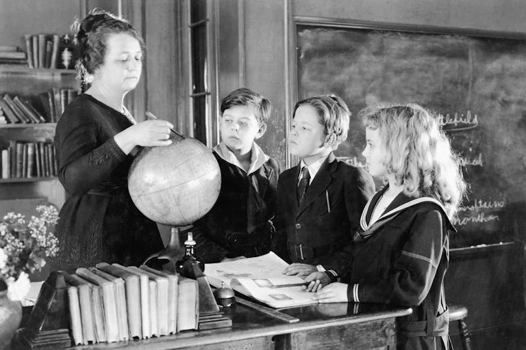 Una maestra enseña geografía con una bola del mundo ante tres alumnos de uniforme.
