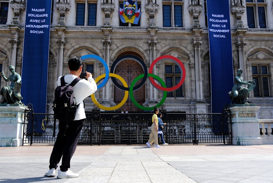 Un homme prend en photo le logo des Jeux olympiques installé devant l'Hotel de ville de Paris