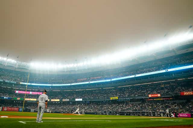 Una neblina marrón anaranjada cubre el estadio iluminado mientras los jugadores saltan al campo en Nueva York.