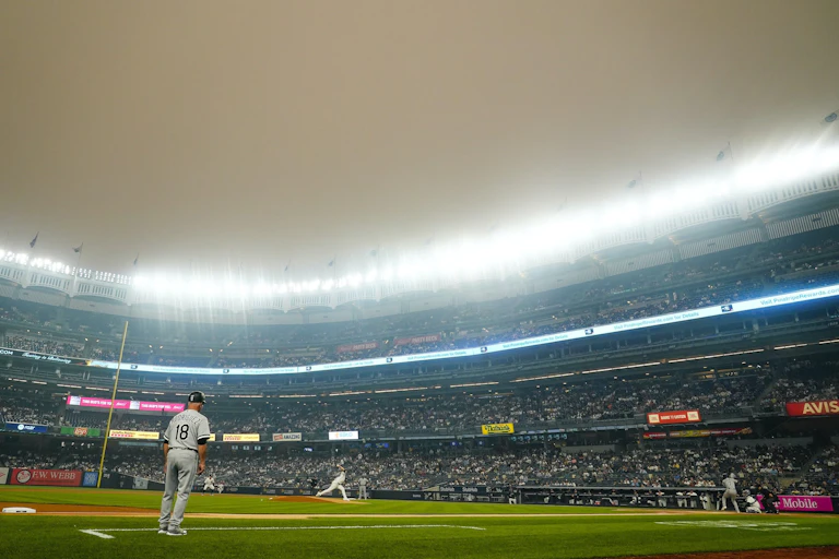 Una neblina marrón anaranjada cubre el estadio iluminado mientras los jugadores saltan al campo en Nueva York.