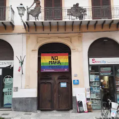 Una puerta en una calle de Palermo en la que hay una bandera arcoíris sobre la que se lee 'No Mafia'.