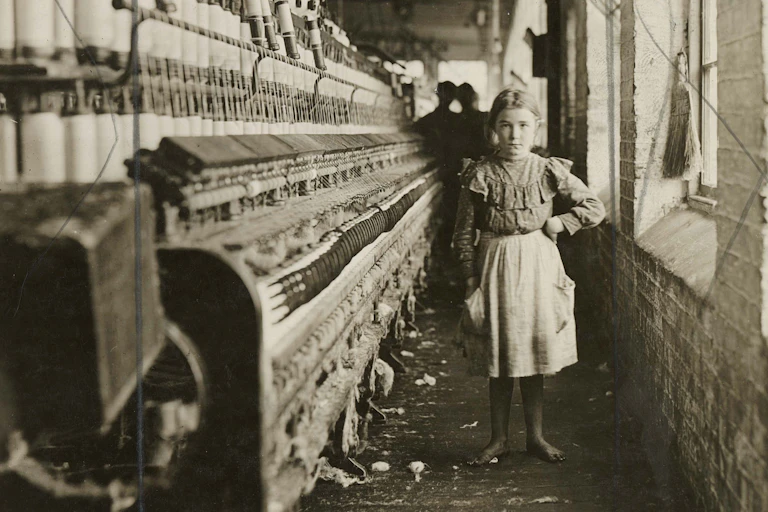 Sepia toned old photograph featuring young girl posing next to looms.