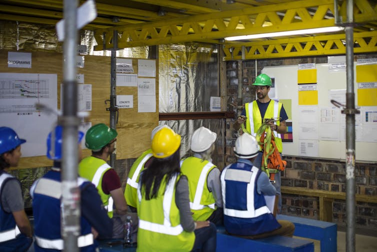 Construction workers wearing hard hats and bright-colored vests getting a safety briefing