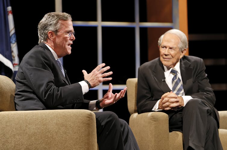 Two men in black suits have a conversation with one another.