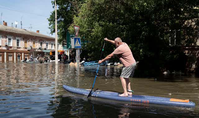 A man on a paddleboard in a flooded street in Kherson, Ukraine, June 2023.