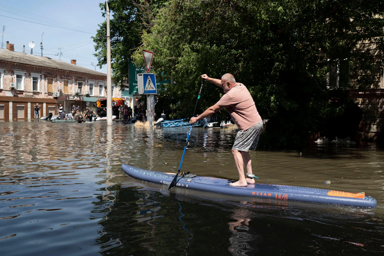 A man on a paddleboard in a flooded street in Kherson, Ukraine, June 2023.