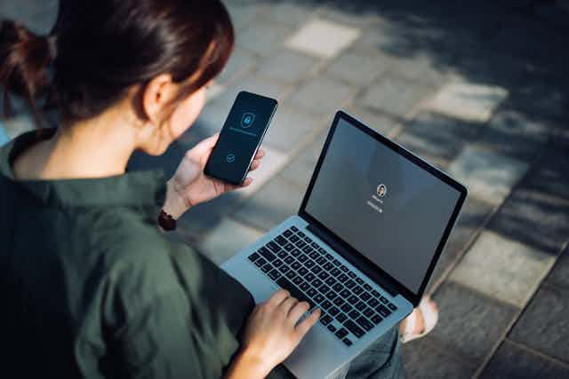Woman holds cellphone while types on laptop