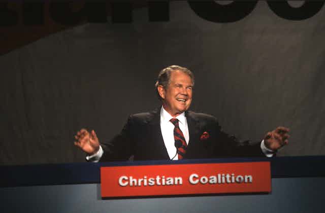 Man in a black suit with a placard in front that says 'Christian Coalition.'