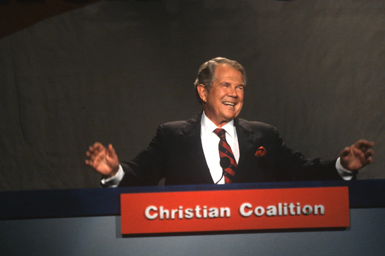 Man in a black suit with a placard in front that says 'Christian Coalition.'