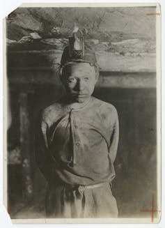 Boy covered in soot poses with his hands clasped behind his back.