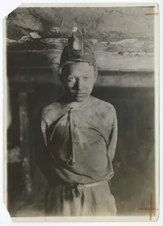 Boy covered in soot poses with his hands clasped behind his back.