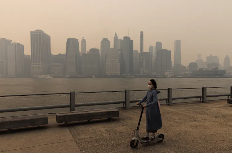 A woman on an electric scooter passes the New York skyline which is engulfed by smoke.