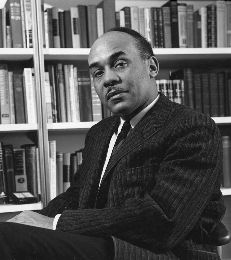 A black-and-white portrait of a man in front of a shelve of books