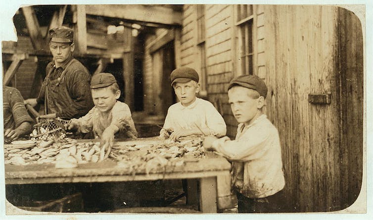 Boys standing at a table splayed with seafood as an older worker obsveres