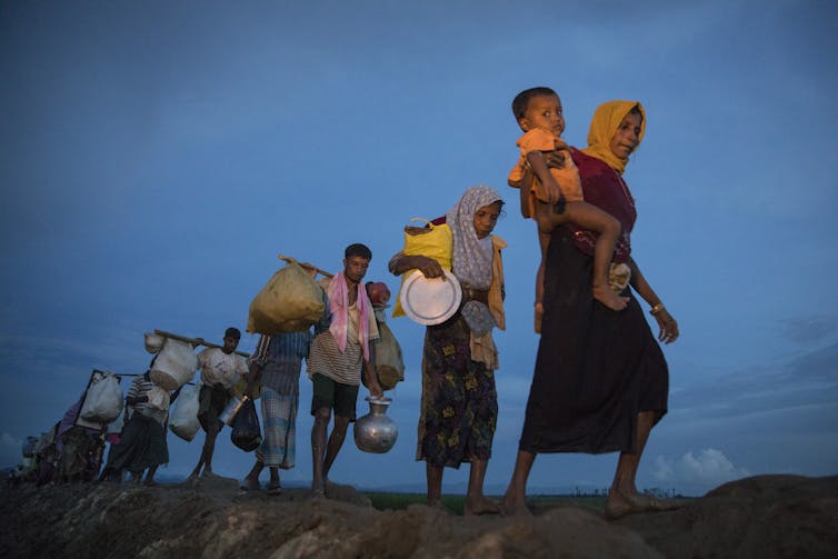 People walk in single file against a dark blue sky.