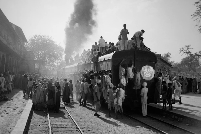 A plume of smoke emerges from the back of a train with people clambering all over the train.