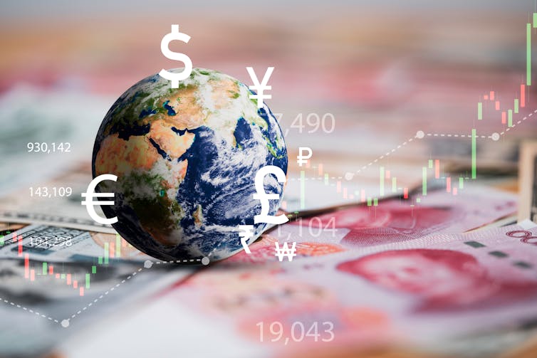 Globe on international banknotes, currency signs including dollar, euro, yen, yuan, pound, financial charts.