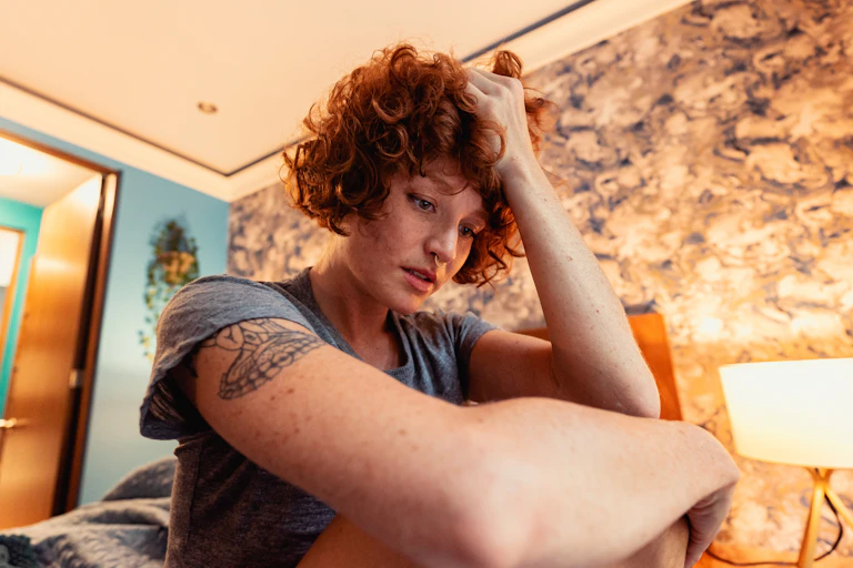 A young woman looks anxious while sitting on her bed.