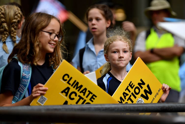 Two primary students hold climate action signs at a rally.