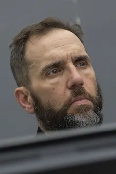 A white man with a beard looks very serious.