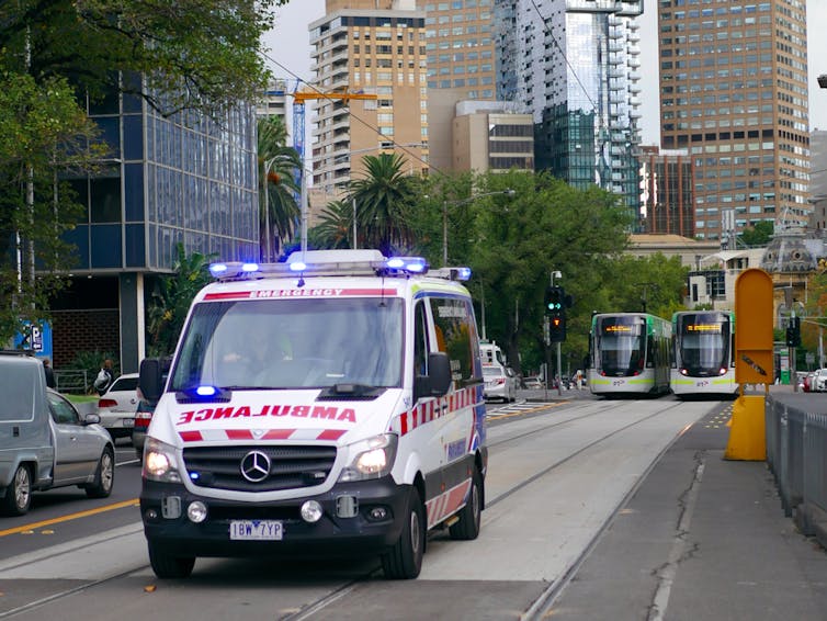 Ambulance driving on tram tracks through Melbourne CBD, trams in background