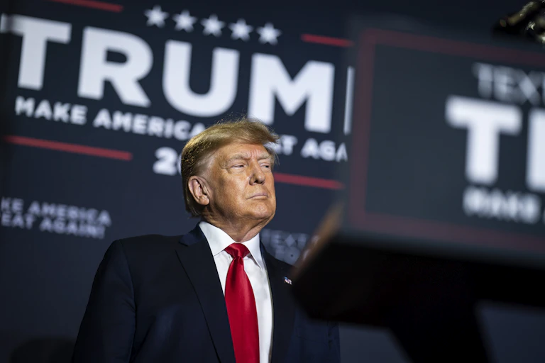A white man dressed in a business suit stands behind a podium with his mouth tightly closed.