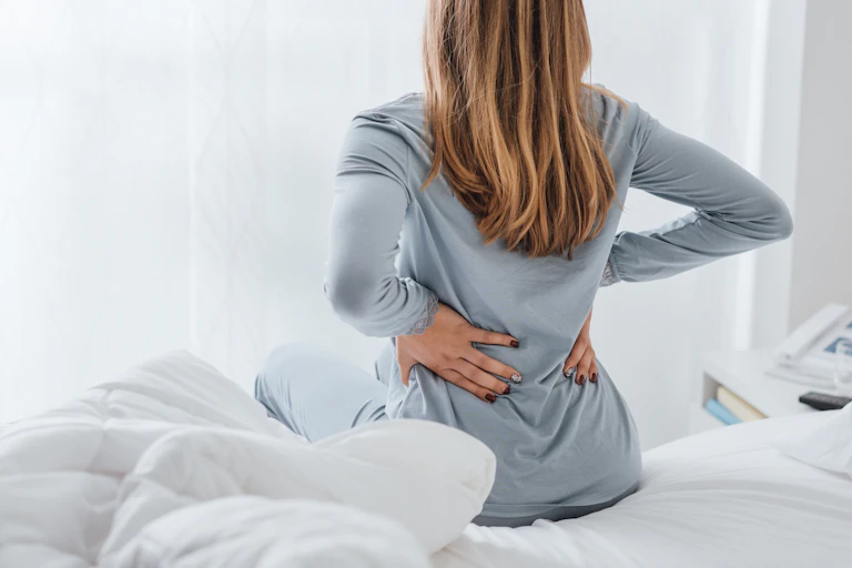 woman sits in bed and rubs lower back