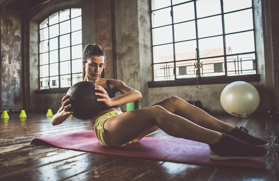 A young woman uses a weighted medicine ball to perform ab exercises in the gym.
