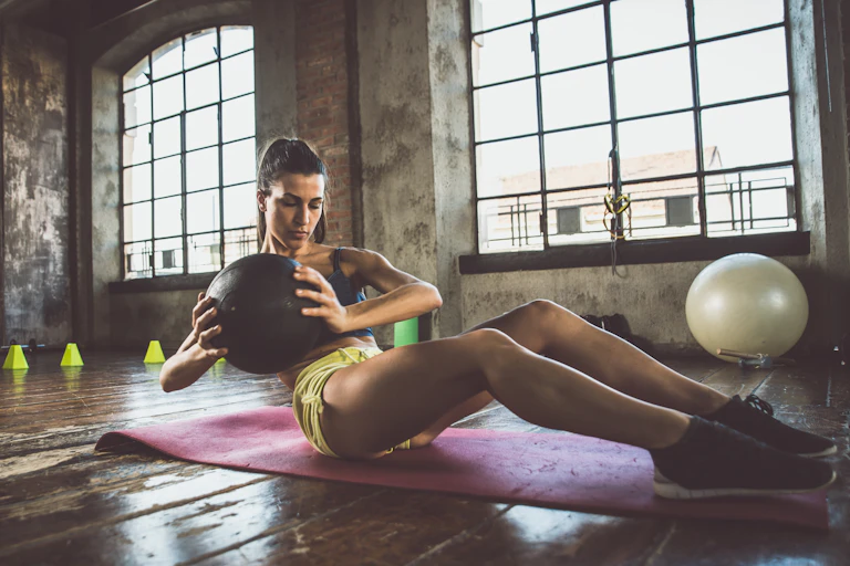 A young woman uses a weighted medicine ball to perform ab exercises in the gym.
