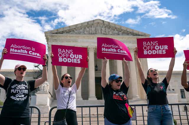 Protesters hold signs supporting abortion access outside a Grecian-style building