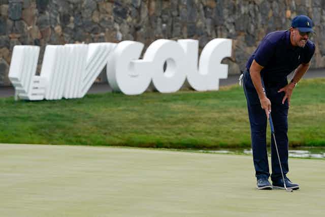 A man holding a golf club leans forward and squints into the distance. A LIV Golf sign is seen in the background.