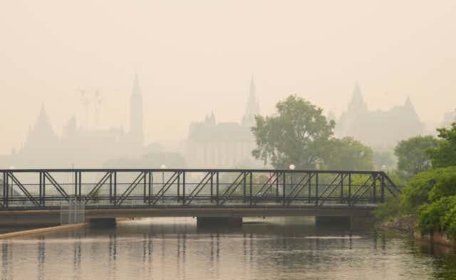 A bridge over water in the foreground with the parliament buildings in the background obscured by smoke