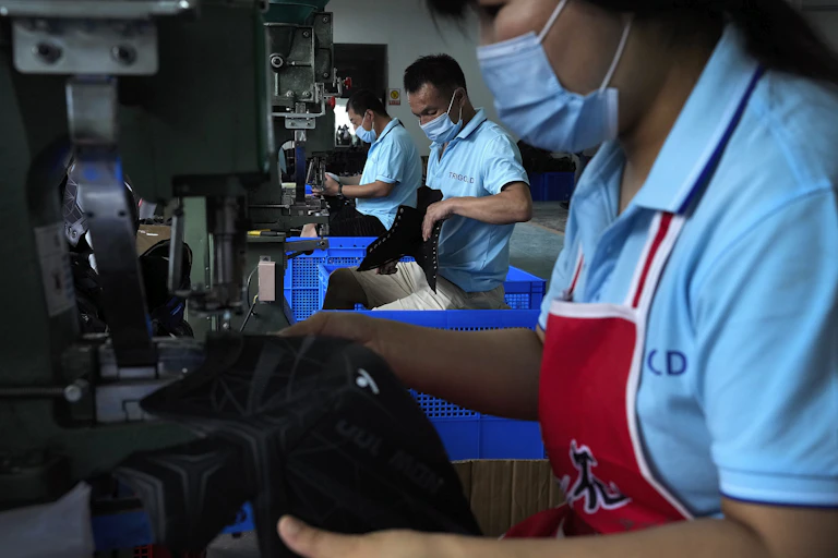 People in medical face masks assemble hockey skates in a factory.