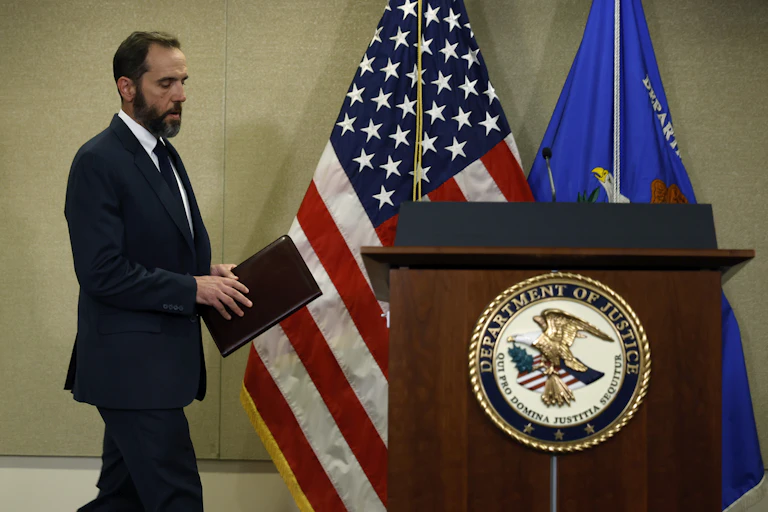 A man dressed in a business suit walks toward a lectern that has an American flag behind it.