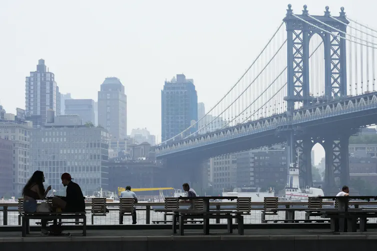 People on benches with a bridge and city view with haze in the background