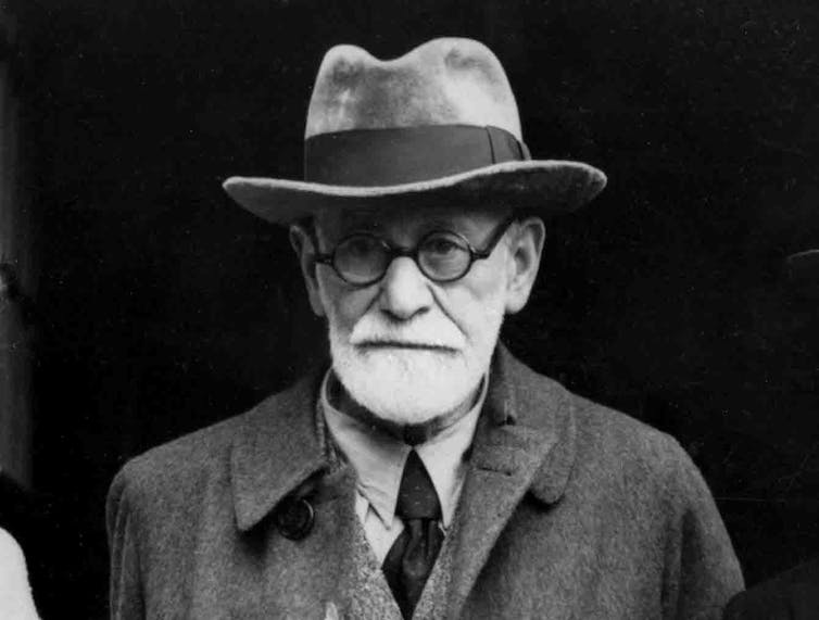 A black-and-white photo of a man with a white beard, round black glasses and a hat.