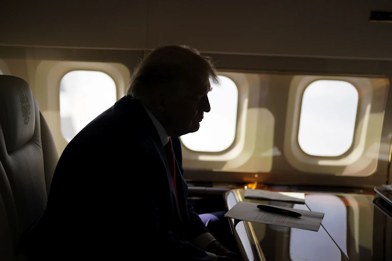 A man obscured in shadow, sitting in front of airplane windows.